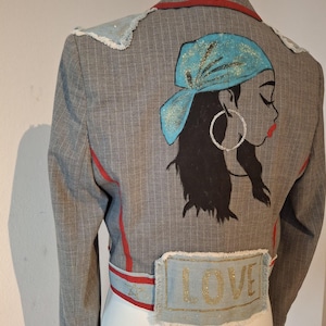 May include: A cropped grey pinstripe blazer with red trim and a blue denim patch on the shoulder. The back of the blazer features a painted design of a woman with a blue headscarf and the word "LOVE" on a blue denim patch.