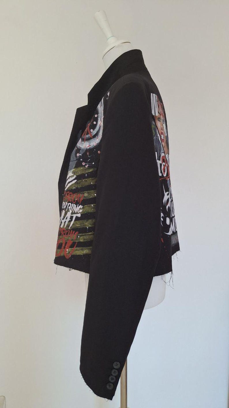 K&ouml;nnte beinhalten: Schwarzer Blazer mit einzigartigem Design. Die Jacke hat eine Collage aus Bildern und Text auf den &Auml;rmeln und dem R&uuml;cken. Der Text enth&auml;lt die W&ouml;rter "Everything" und "What". Der Blazer hat einen klassischen Kragen und vier Kn&ouml;pfe am &Auml;rmel.