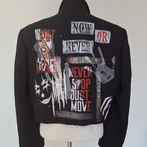 K&ouml;nnte beinhalten: Schwarze Jacke mit bemalten Kunstwerken und Text. Auf der R&uuml;ckseite der Jacke stehen die Worte "NOW OR NEVER", "NEVER STOP JUST MOVE" und "WHAT LOVE". Ein Handabdruck und ein Gesicht sind ebenfalls auf die Jacke gemalt.