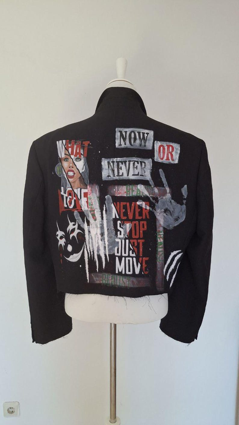 K&ouml;nnte beinhalten: Schwarze Jacke mit bemalten Kunstwerken und Text. Auf der R&uuml;ckseite der Jacke stehen die Worte "NOW OR NEVER", "NEVER STOP JUST MOVE" und "WHAT LOVE". Ein Handabdruck und ein Gesicht sind ebenfalls auf die Jacke gemalt.