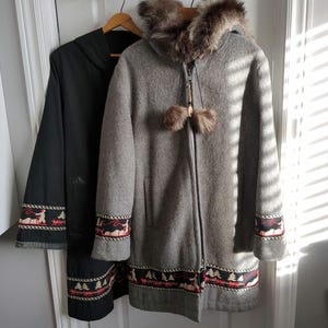 Puede incluir: Dos abrigos de invierno colgando de una puerta. Uno es gris con capucha forrada de piel y adornos decorativos con renos y árboles. El otro es negro con adornos similares. Ambos tienen perchas de madera.