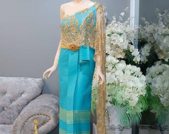 May include: A turquoise one-shoulder dress featuring a gold lace overlay on the bodice and a matching gold belt. The skirt is a long, straight-cut piece with a subtle geometric pattern and horizontal gold bands near the hem, paired with a long gold lace shawl.
