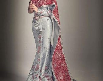 May include: A floor-length silver gown featuring a one-shoulder neckline and a long, draped red sash with intricate rose embroidery. The dress includes a fitted bodice with a pleated waist detail and a skirt adorned with matching red rose patterns.