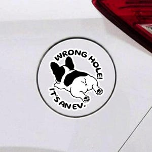 May include: A circular white vinyl decal featuring a black and white illustration of a French Bulldog viewed from behind. The text WRONG HOLE! IT'S AN EV! is printed in black capital letters in a curved arc around the dog illustration.