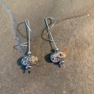 May include: A pair of silver earrings with a unique, twisted design. Each earring features a small, round, speckled stone.
