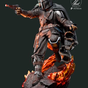 Puede incluir: Estatua detallada de un guerrero mandaloriano con armadura oscura, sosteniendo una pistola bl&aacute;ster con una luz roja. La figura se alza sobre una base rocosa con acentos de color naranja y amarillo fuego. Una peque&ntilde;a criatura verde est&aacute; sobre el hombro del guerrero.