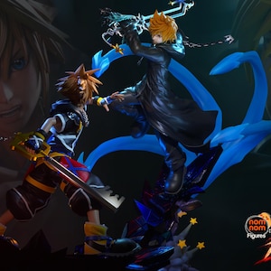 May include: A dynamic figurine set featuring two characters with spiky blonde hair in a combat pose. One character wears a black and blue outfit with a yellow-handled sword, while the other wears a black coat and wields a glowing blue weapon.