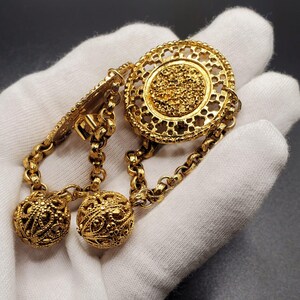 May include: A gold-toned chain necklace with two round, ornate pendants and a large, circular pendant with a filigree design.