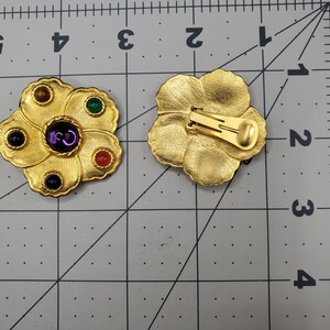 May include: A pair of gold tone clip-on earrings with a flower design. The earrings have five colorful stones set in the flower petals. The back of the earrings have a simple clip closure.