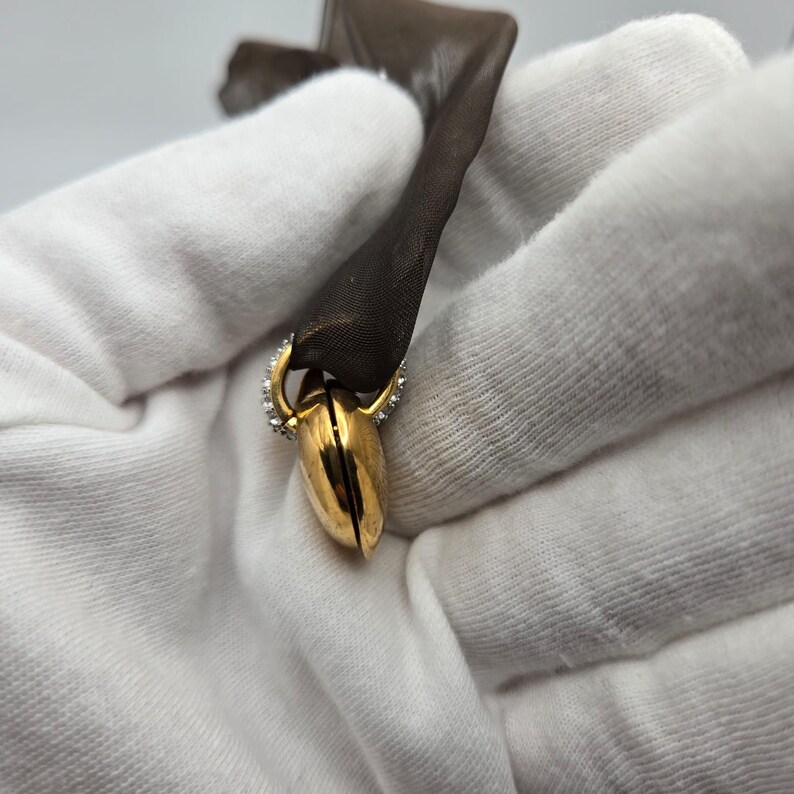 May include: A gold heart-shaped pendant with a small opening on one side. The pendant is decorated with small, clear stones around the edge.
