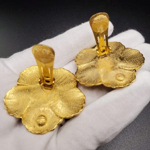May include: A pair of gold-tone flower-shaped clip-on earrings. The earrings have a textured surface and a detailed design.