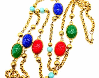 Puede incluir: Un collar de cadena dorada con cuentas ovaladas de color verde, azul y rojo. Cada cuenta tiene un diseño tallado y está separada por pequeñas cuentas doradas. También hay cuentas de color azul turquesa intercaladas en la cadena.