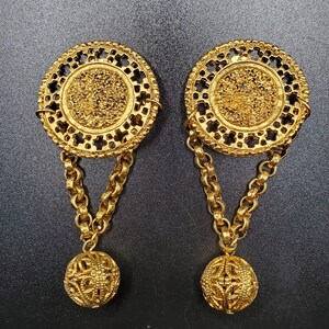 May include: A pair of gold-tone dangle earrings with a round, openwork design and a dangling ball at the end of each earring.
