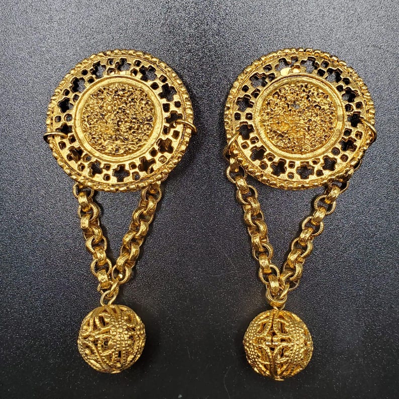 May include: A pair of gold-tone dangle earrings with a round, openwork design and a dangling ball at the end of each earring.