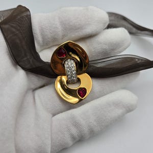 May include: Gold-tone heart-shaped brooch with a clear crystal-encrusted ring and two red heart-shaped stones.