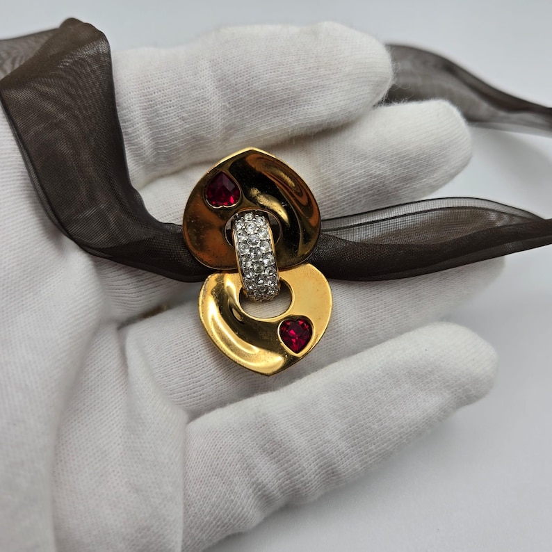 May include: Gold-tone heart-shaped brooch with a clear crystal-encrusted ring and two red heart-shaped stones.