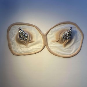 May include: Two white fabric shapes with a raised, textured surface and a cluster of iridescent rhinestones on each.