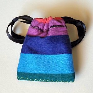 May include: A small, colorful drawstring bag with a rainbow striped pattern. The bag has a black drawstring and is made of fabric.