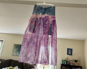 Puede incluir: Una falda larga y fluida con un estampado tie-dye morado y blanco. La falda está superpuesta a unos pantalones cortos de mezclilla con ribete de encaje.