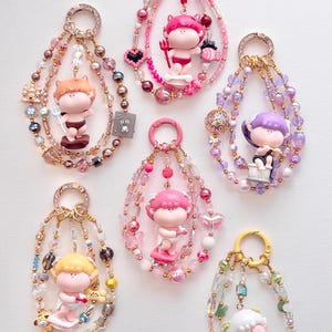 May include: Six colorful beaded keychains with small figurines of cherubs holding different objects. Each keychain features a different color scheme and bead pattern.