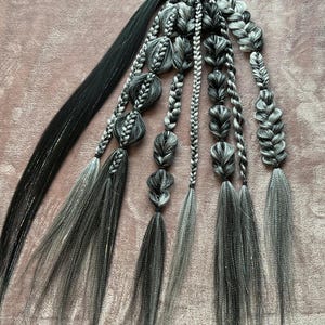 May include: A set of black and silver hair extensions with a black elastic band. The extensions are braided and have a ombre effect, transitioning from black to silver.
