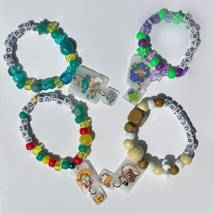 May include: Four beaded bracelets with charms. One bracelet is teal and green with the word "EFFORT". Another is purple and green with the word "HYDRANGEA". The third is red, yellow, and green with the word "LANGUE". The last is brown and white with the word "CAPPUCCINO".