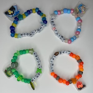 May include: Four beaded bracelets with charms. One is blue and yellow with the word "MOONLIGHT". Another is pink and blue with the words "SEA FAIRY". A third is green with "WIND ARCHER". The last is orange with "FIRE SPIRIT".