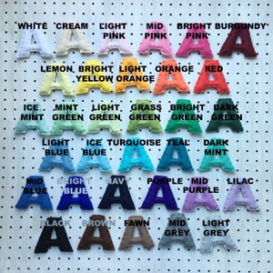 May include: A collection of felt letter "A" shapes in various colors, including pink, blue, green, and purple. Each letter is displayed against a white pegboard background, with color names above each letter.