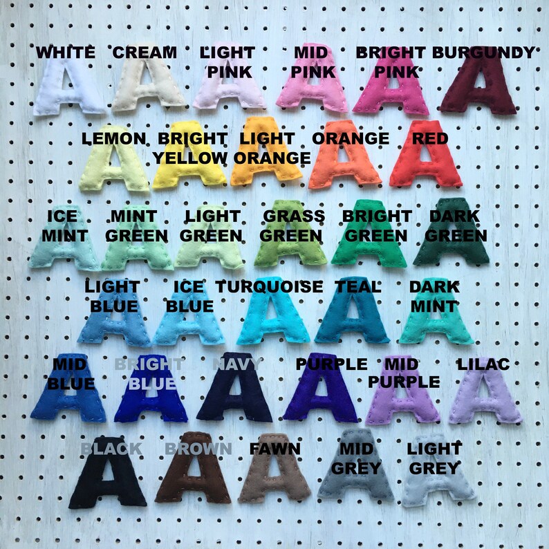 May include: A collection of felt letter "A" shapes in various colors, including pink, blue, green, and purple. Each letter is displayed against a white pegboard background, with color names above each letter.