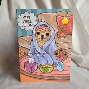 Könnte beinhalten: Eine Gute-Besserung-Karte mit einem Cartoon-Chihuahua, der in eine blaue Decke gewickelt ist, eine Schlafmaske trägt und ein Thermometer hält. Der Chihuahua sitzt auf einem Sofa mit einem Teddybär und einem gelben Ballon. Die Karte enthält auch eine Schüssel Suppe, Taschentücher und Blumen.