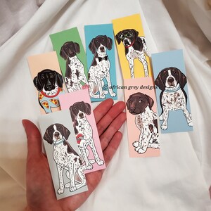 May include: Set of eight illustrated bookmarks featuring different poses of German Shorthaired Pointers. Each bookmark is printed on a different colored background.