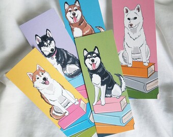 May include: Five colorful bookmarks featuring different husky dog breeds sitting on stacks of books. Each bookmark has a different colored background and a different breed of husky dog.
