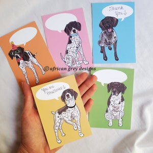 May include: Greeting cards featuring illustrations of a German Shorthaired Pointer dog. Each card has a different background color and a speech bubble. One card says "Thank You!" and another says "You are PAWSOME!"