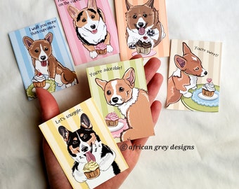 May include: Five illustrated greeting cards featuring a cartoon corgi dog with different cupcake-themed messages. The messages include "I wuff you more than cupcakes", "You're the king on the cupcake", "You're adorable", "You're my best friend", and "You're sweet!"