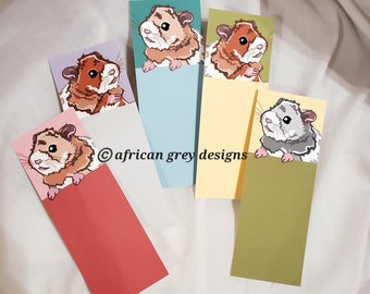May include: A collection of colorful bookmarks featuring illustrations of hamsters. Each bookmark has a different colored background, including pink, blue, yellow, and green. The text "african grey designs" is printed on the bookmarks.