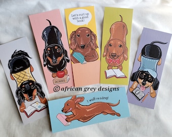 May include: Set of five illustrated bookmarks featuring dachshund dogs reading books. The bookmarks are printed on cardstock and have a matte finish. The text on the bookmarks includes "Let's curl up with a good book!" and "I wuff reading!"