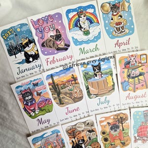K&ouml;nnte beinhalten: Eine Sammlung von illustrierten Monatskalenderkarten mit skurrilen Katzendesigns. Jede Karte zeigt den Namen eines Monats und eine einzigartige Katzenillustration, mit Themen wie Winter, Regenbogen und Spa-Tagen. Die Karten sind mit lebendigen Farben und verspielten Details versehen.