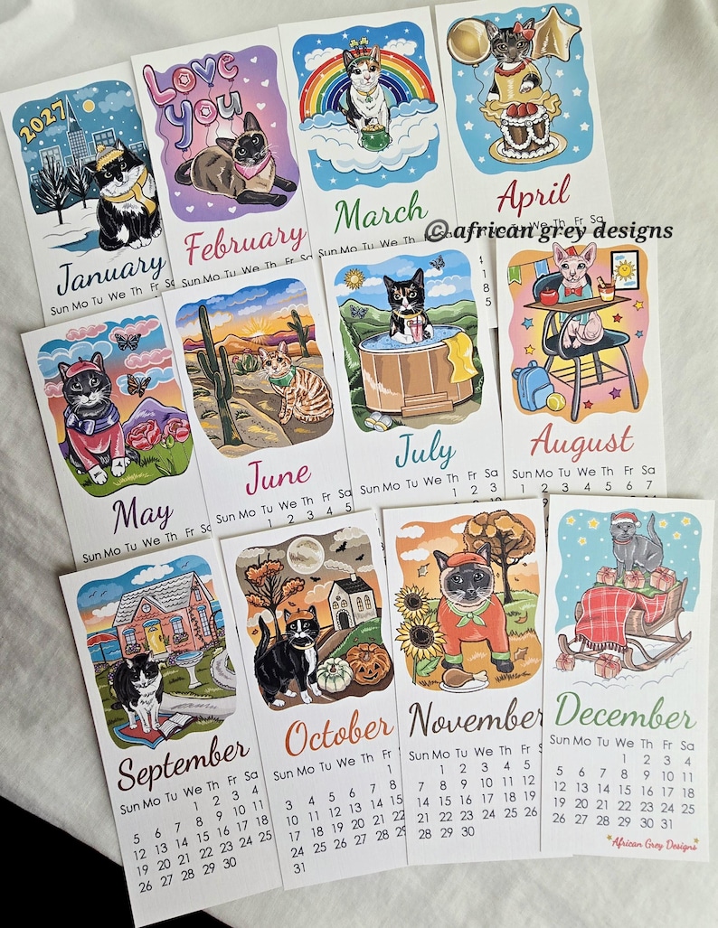 K&ouml;nnte beinhalten: Ein 2027-Kalender mit monatlichen Illustrationen von Katzen in verschiedenen Umgebungen. Jeder Monat zeigt eine einzigartige Szene mit Katzenmotiven, mit Daten und Wochentagen. Der Kalender enth&auml;lt den Text "African Grey Designs".