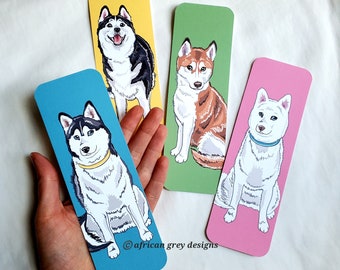May include: Four colorful bookmarks featuring illustrations of Siberian Huskies. Each bookmark has a different colored background: yellow, green, pink, and blue. The bookmarks are all the same size and shape, and they feature the text "@african grey designs" in the bottom right corner.