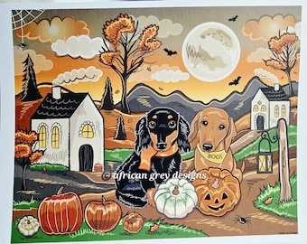 May include: A Halloween-themed print featuring two dachshunds, pumpkins, and a full moon. One dog wears a scarf, the other a "BOO!" bandana. The artwork includes houses, trees, and bats against an orange and brown sky.