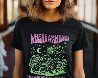 May include: Black t-shirt with a graphic design featuring the text "WHERE AS MY MIND" in pink, along with green frogs, mushrooms, and celestial elements. The text "CALIFORNIA FORAGING COLLECTIVE" is also included.