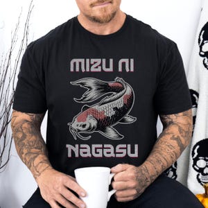 Peut inclure: T-shirt noir avec un motif de carpe koï et du texte japonais. Le texte "Mizu Ni Nagasu" est en rose et blanc. La carpe koï est rouge, blanche et noire. Le t-shirt est à col rond.