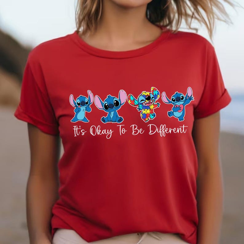 May include: Red t-shirt featuring four blue cartoon characters with the text "It's Okay To Be Different". The characters are in different poses, with one character having a colorful, puzzle-like design.