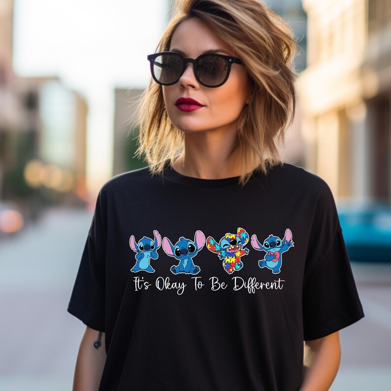 May include: Black t-shirt featuring four cartoon Stitch characters in various colors. The text "It's Okay To Be Different" is printed below the characters. The shirt is worn by a person wearing sunglasses.