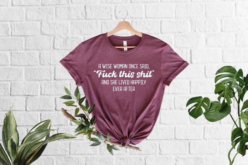 May include: A maroon t-shirt with the text 'A wise woman once said, 'Fuck this shit' and she lived happily ever after' printed in white on the front.