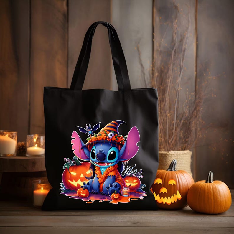 May include: A black tote bag featuring a graphic print of a blue alien character wearing a striped witch hat and orange scarf. The character is surrounded by carved jack-o'-lantern pumpkins, a small bat, and a skull, all set against a dark background.