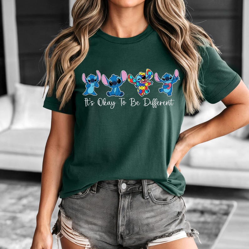 May include: Dark green t-shirt featuring a graphic of the character Stitch in various designs. The text "It's Okay To Be Different" is printed below the characters in white. The shirt is made of a soft material.