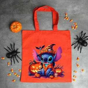 May include: A bright orange tote bag featuring a graphic of a blue alien character wearing a witch hat adorned with orange flowers and a small skull. The character is surrounded by jack-o'-lanterns, a small bat, and a jar on a dark background.