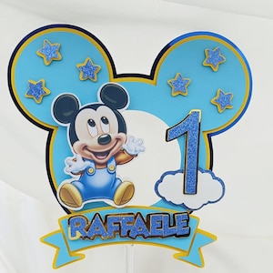 Puede incluir: Adorno para tarta con temática de Mickey Mouse para un primer cumpleaños. El diseño azul y amarillo presenta a Mickey Mouse, el número 1 y el nombre "RAFAELE". Estrellas y detalles brillantes añaden un toque festivo.