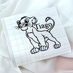 Op de afbeelding: Zwart-witte illustratie van een leeuwenwelp met de naam "Tiago" eronder. De afbeelding is op een transparante achtergrond met een rasterpatroon.